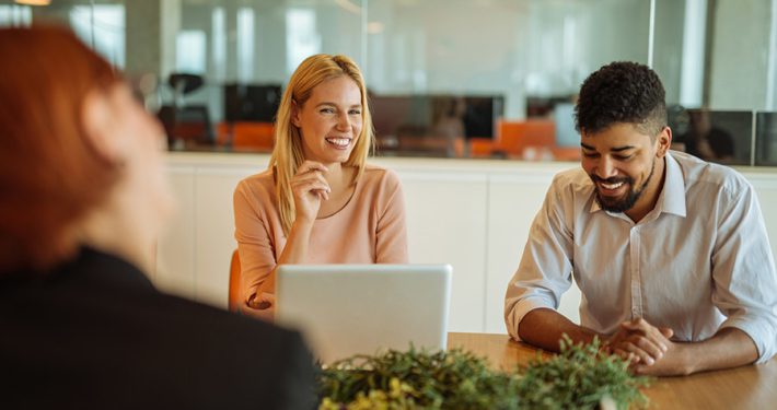 Three people sitting around a table in an office with one person smiling and listening in a demonstration of leading with empathy