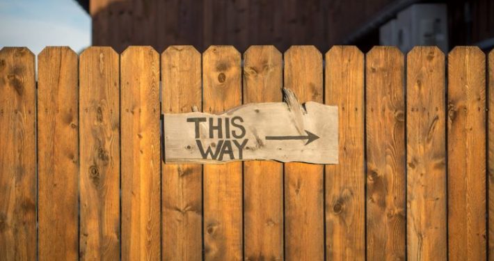 Brown wooden fence with sign that reads "This Way" with an arrow to online leadership training benefits.