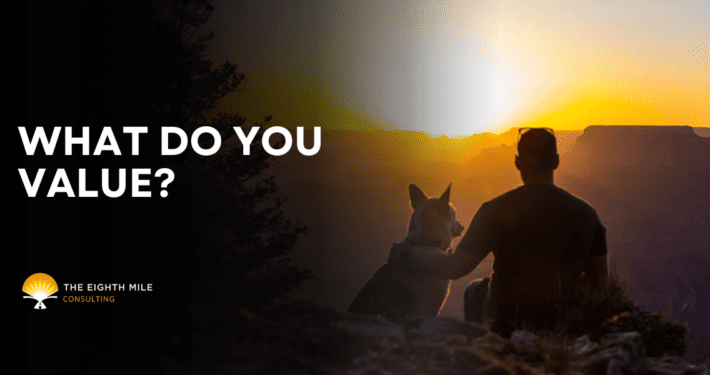 A person with their dog gazes into a glowing sunset over a mountain ridge while contemplating values in business.